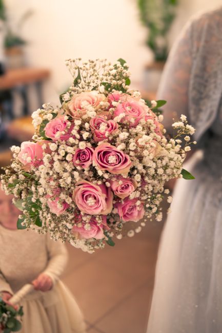 A close-up of a floral bouquet featuring pink roses and white baby's breath, arranged in a rounded, lush style. The roses have soft petals with a gentle gradient from deeper pink at the center to ligh